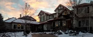 A snowy two-story house at sunset with red and white lights along the roof lines