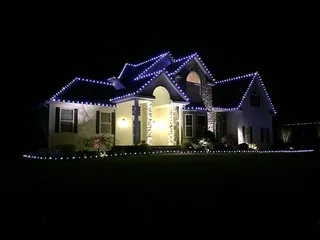 A house at night with blue and white lights along the roof lines and the walkway