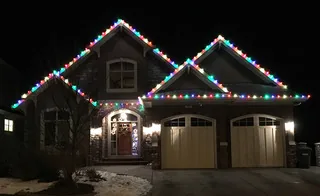 A house at night with multicolor lights along the roof lines and over the garage