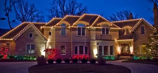 A large stone two-story house at night with multicolor lights along every roof line