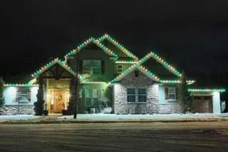 A stone house at night with green and warm white lights along the roof lines