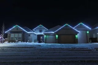 A house in snow at night with white lights along the roof and green accents at the corners