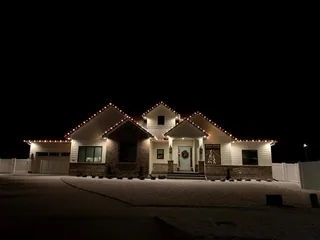 A house at night with red and warm white lights along the roof lines and a lit walkway