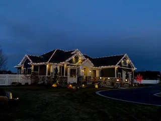 A ranch house at dusk with red and white lights along the roof lines and porch