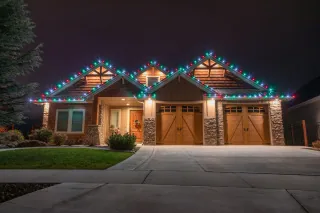 A craftsman house at night with red, white and green lights along the roof and over the garage