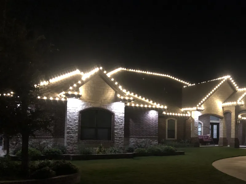 A brick ranch house at night with warm white lights along every roof line and gable