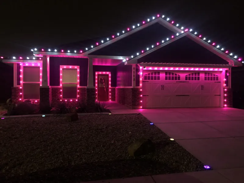 A ranch house at night outlined in pink and white lights along the roof, around the windows and across the garage