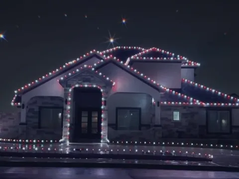 A stone and stucco house at night with red and white lights along the roof lines, the entry and the edge of the driveway